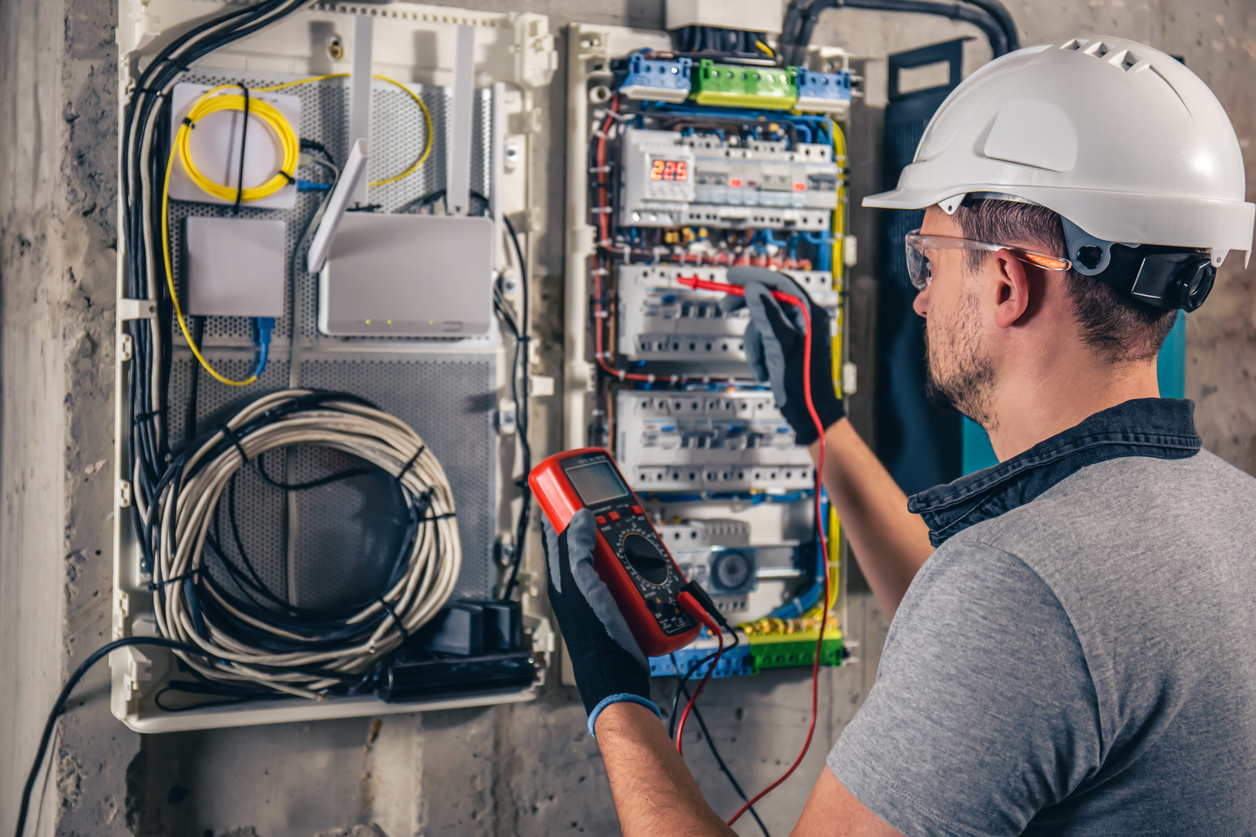 A male electrician works in a switchboard with an electrical connecting cable.